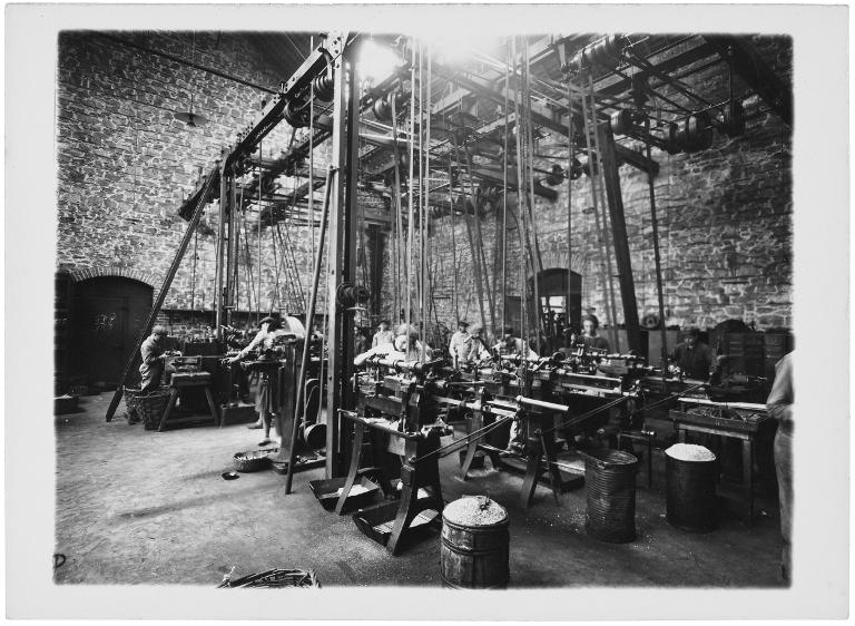 Saint-Brieuc, usine Chaffoteaux. Vue d’une machine industrielle avec plusieurs postes de travail pour les ouvriers, parmi lesquels se trouvent des femmes et de jeunes garçons. Photographie prise par Raphaël Binet (1880-1961), 2e moitié du 20e siècle – Licence CC-BY-SA – Collection du Musée de Bretagne, Rennes.